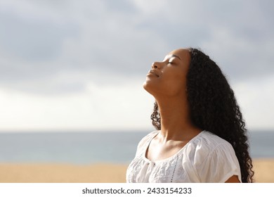 Black woman breathing fresh air on the beach a cloudy day - Powered by Shutterstock