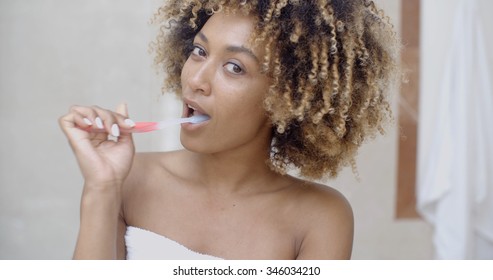 Black Woman Brushing Her Teeth And Smiling In The Bathroom