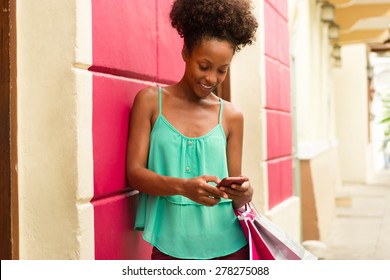 Black Woman In Casco Antiguo - Panama City With Shopping Bags. The Girl Leans On A Wall And Types Message With Her Phone On Social Network. 