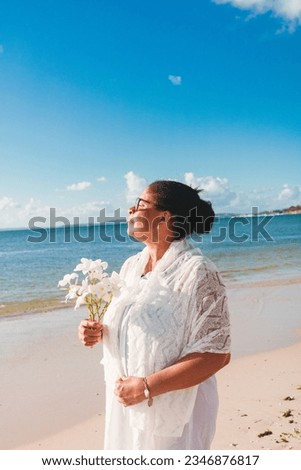 Black woman celebrating February 2nd, Yemanja festival, tossing flowers on the beach. Brazil traditional celebration 