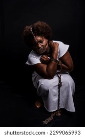 Black woman in chains with an iron mask on her face, representing the slave Anastacia. Pain and suffering, torture. Against black background.