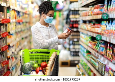 Black Woman Checking Expiration Date On Food Product Doing Grocery Shopping In Supermarket Groceries Store, Standing In Aisle With Shop Trolley. Lady Buyer Choosing Healthy Food Concept