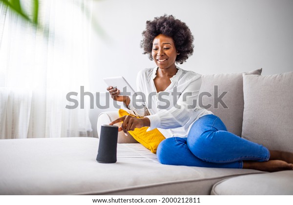 Black\
woman connecting phone to her virtual assistant smart speaker.\
Happy black woman using smart speaker at home. Young cheerful woman\
controlling home devices with a voice\
commands