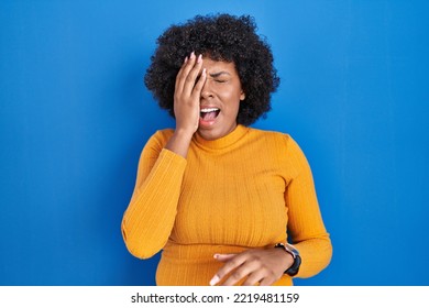 Black Woman With Curly Hair Standing Over Blue Background Yawning Tired Covering Half Face, Eye And Mouth With Hand. Face Hurts In Pain. 