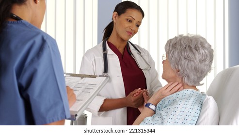 Black Woman Doctor Holding Elderly Patient's Hand In Hospital Room