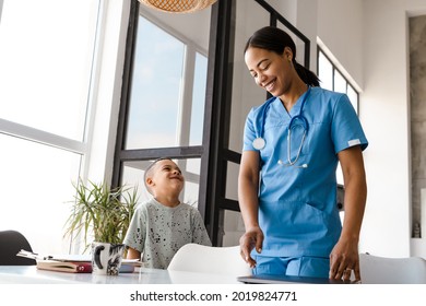 Black Woman Doctor Laughing With Her Son While Standing At Table In Home