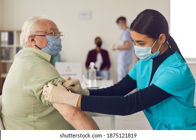 Black Woman Doctor Nurse In Medical Uniform And Protective Mask Making Vaccination With Syringe Against Covid-19 Virus For Senior Elderly Man Patient During Pandemic In Medical Clinic Office