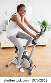 Black Woman Doing Exercise Bike With Headphones In A Living Room