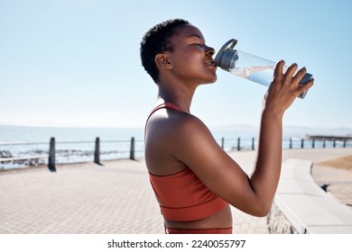 Black woman, drinking water or bottle in fitness workout, training or exercise by beach, ocean or sea in summer location. Smile, happy or sports runner with drink for healthcare wellness recovery - Powered by Shutterstock