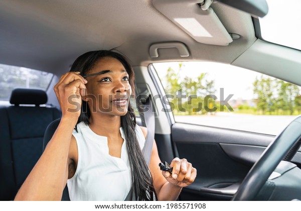 A black woman driver seated in her new car holding\
make up