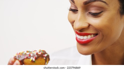 Black Woman Eating Chocolate Donut With Sprinkles And Smiling