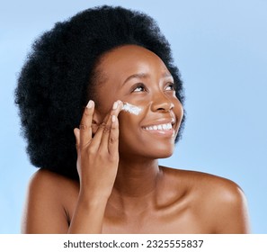 Black woman, face and cream, beauty and skincare with cosmetics on blue background. Moisturizer, lotion and product for skin with sunscreen and happiness, female model and dermatology in studio