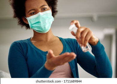 Black Woman With Face Mask Using Hand Sanitizer At Home During Virus Pandemic. 