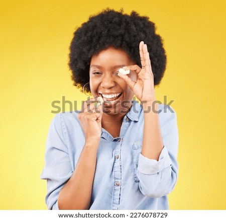 Black woman, funny face and eating popcorn in studio isolated on a yellow background. Comic smile, food and portrait of laughing, hungry and happy, goofy or silly female playing with corn or snack.