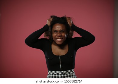 The black woman is furious. A black woman in a black sweater with a neckline furiously and emotionally pulls her hair.