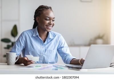 Black Woman Graphic Designer Working With Color Swatches And Laptop At Modern Office, Looking At Computer Screen, Free Space