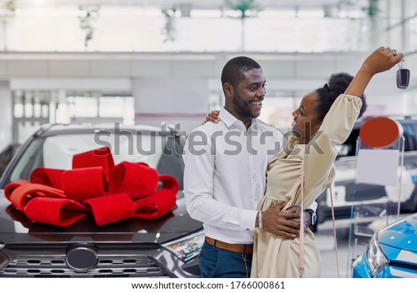 black woman is happy after getting a car by\
her husband, she looks at him with love and gratitude. new\
automobile with red bow in the\
background