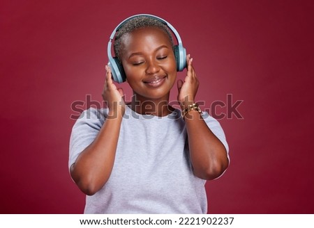Black woman, headphones and smile for music listening, streaming or relax against a studio background. African American female with smile enjoying audio track, hifi or relaxing with wireless headset