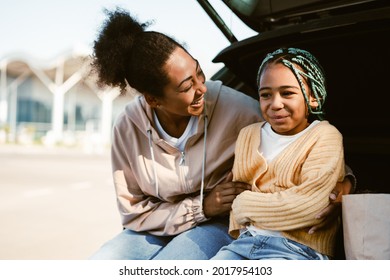 Black Woman And Her Daughter Laughing And Hugging While Sitting In Car Trunk