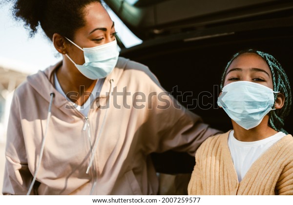 Black woman and her daughter putting on face\
masks outdoors