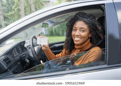 Black woman holding up driving license to her first new car. Customer satisfaction