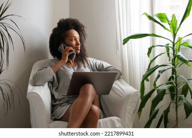 Black woman at home using laptop for working from home while doing a phone call. - Shutterstock ID 2217899431
