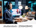 Black woman immersed in world of technology, wearing wireless headphones as she edits photos and videos. African american female filmmaker working with footage and sound, editing new project.