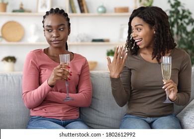 Black woman jealous of her friends engagement ring, drinking champagne together, home interior