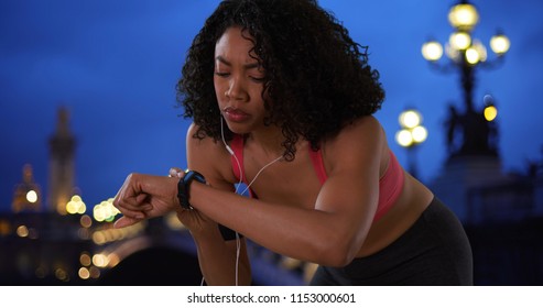 Black Woman Jogger Checking Fitness Tracker While On A Night Run In Paris