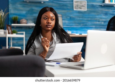 Black woman looking at accounting strategy on monitor using laptop computer remote working at financial graph planning presentation. African american student analyzing infographics document at home
