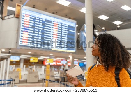Black woman looks at the flight schedule on a digital monitor in an airport to check the gate and time to board the plane to travel or study abroad.