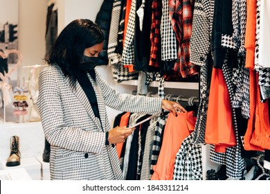 Black Woman Manager In A Fashion Retail Store Is Wearing A Mask As Protection Against Virus And Using A Tablet For Working And Checking The Shop Stock