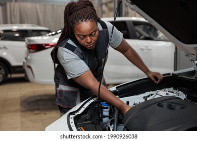 Black Woman Mechanic Working Under The Hood At Repair Garage. Portrait Of Confident Focused Mechanic Woman Working Ona Car In An Auto Repair Shop. Female Mechanic Working On Car. Side View