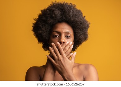 black woman on yellow background with hand in mouth, concept of abuse, feminicide, racism and prejudice