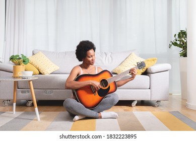 Black Woman Playing Guitar Sitting On Floor In The Living Room Of Her House