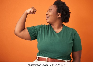 Black woman, power and smile in orange background with arm flex for leader, gender equality and confident. Happy, proud and fist of girl for success, tough and strength in studio for empowerment - Powered by Shutterstock