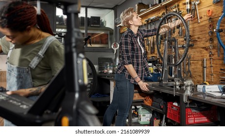 Black Woman Repairman Fixing Electric Scooter While Her Female Caucasian Colleague Taking Wrench For Work In Modern Workshop. Bike Service, Repair And Upgrade. Garage Interior With Tools And Equipment