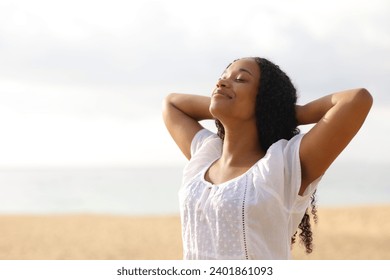 Black woman resting breathing fresh air with hands on head on the beach a cloudy day - Powered by Shutterstock