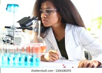 Black Woman Scientist Student Chemist In Protective Goggles Are Conducting Research Using Microscope For Bacterial Contamination Of Water To Search For Vaccine To Treat Diseases In Medicine.