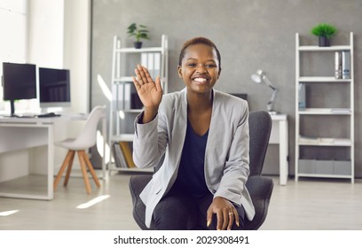 Black Woman Sitting In Office, Waving Hand, Smiling And Saying Hello. Laptop Computer Screen View Of Business Expert Greeting You In Videochat, Distance Learning Videocall, Educational Videoconference