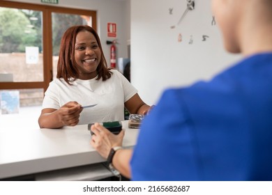 A black woman smiles with joy holding her credit card before paying in return for the good service she has received at the dental clinic - Powered by Shutterstock