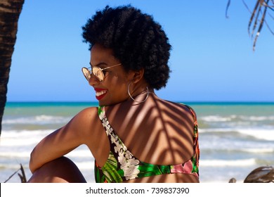 Black woman smiling in the beach with a coconut tree shadow at her back