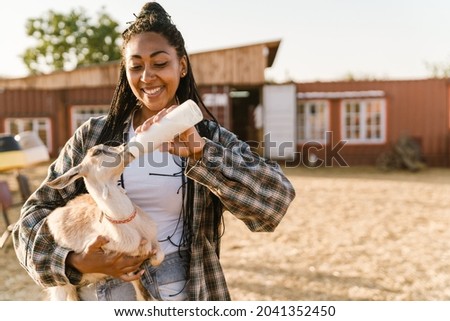 Black woman smiling and feeding goat while working on farm outdoors