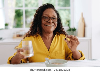 Black woman smiling as she adds vitamin supplements to her breakfast to support her health. Mature woman enjoying a balanced diet, taking extra care to ensure she's getting all the nutrients she needs - Powered by Shutterstock