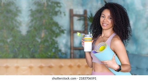 Black Woman In Sportswear Drinking Water From Bottle In Loft Fitness Studio Gym Looking At Camera, Holding Yoga Mat. In Blue Indoor With Many House Plants. Copy Space Banner.