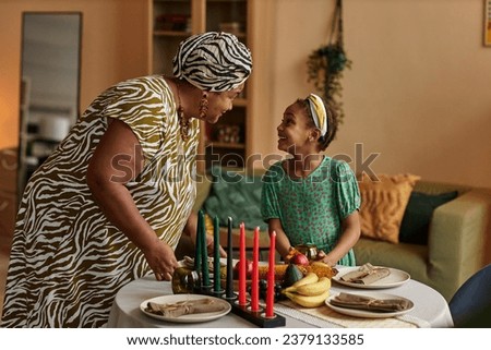 Black woman in traditional clothes explaining granddaughter origins of kwanzaa holiday