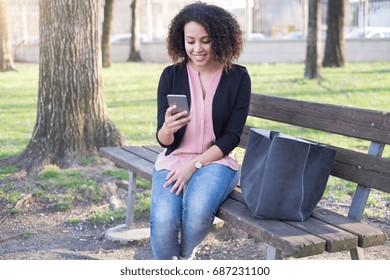 Black Woman Using App On Mobile Phone In The City Park