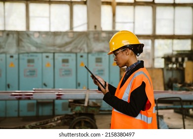 Black Woman Wearing Helmet Using Tablet Computer While Working At Factory Indoors