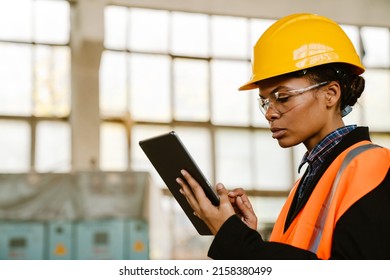 Black Woman Wearing Helmet Using Tablet Computer While Working At Factory Indoors