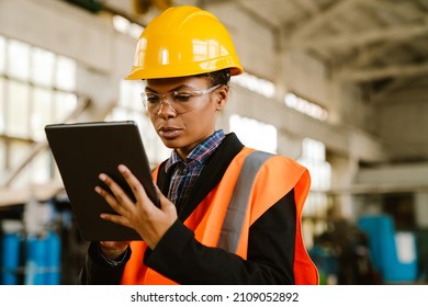 Black Woman Wearing Helmet And Vest Working With Tablet Computer At Factory